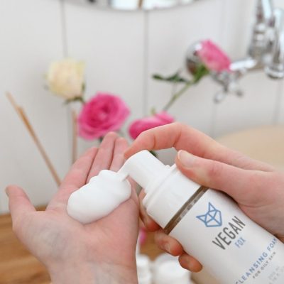 Vegan Fox vegan cleansing foam for oily skin being dispensed into hand with flowers in background